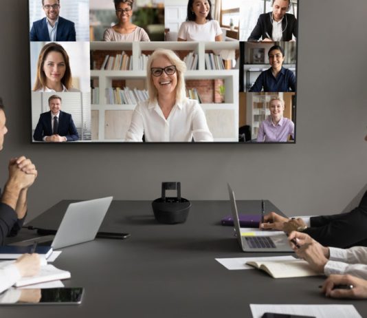Riunione aziendale ibrida con partecipanti in sala e in videoconferenza su grande schermo in video HD, grazie a una telecamera per conferenze professionale Marmitek