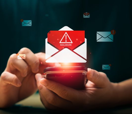 L’importanza del test del dominio: come difendersi da spoofing e attacchi email Persona che utilizza uno smartphone mentre compare un’icona di allerta malware su un’email, simbolo dei rischi legati al phishing e alla necessità del test del dominio per proteggere l’identità digitale aziendale