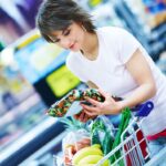 Portrait of a happy young woman with her purchased grocery items in a cart
