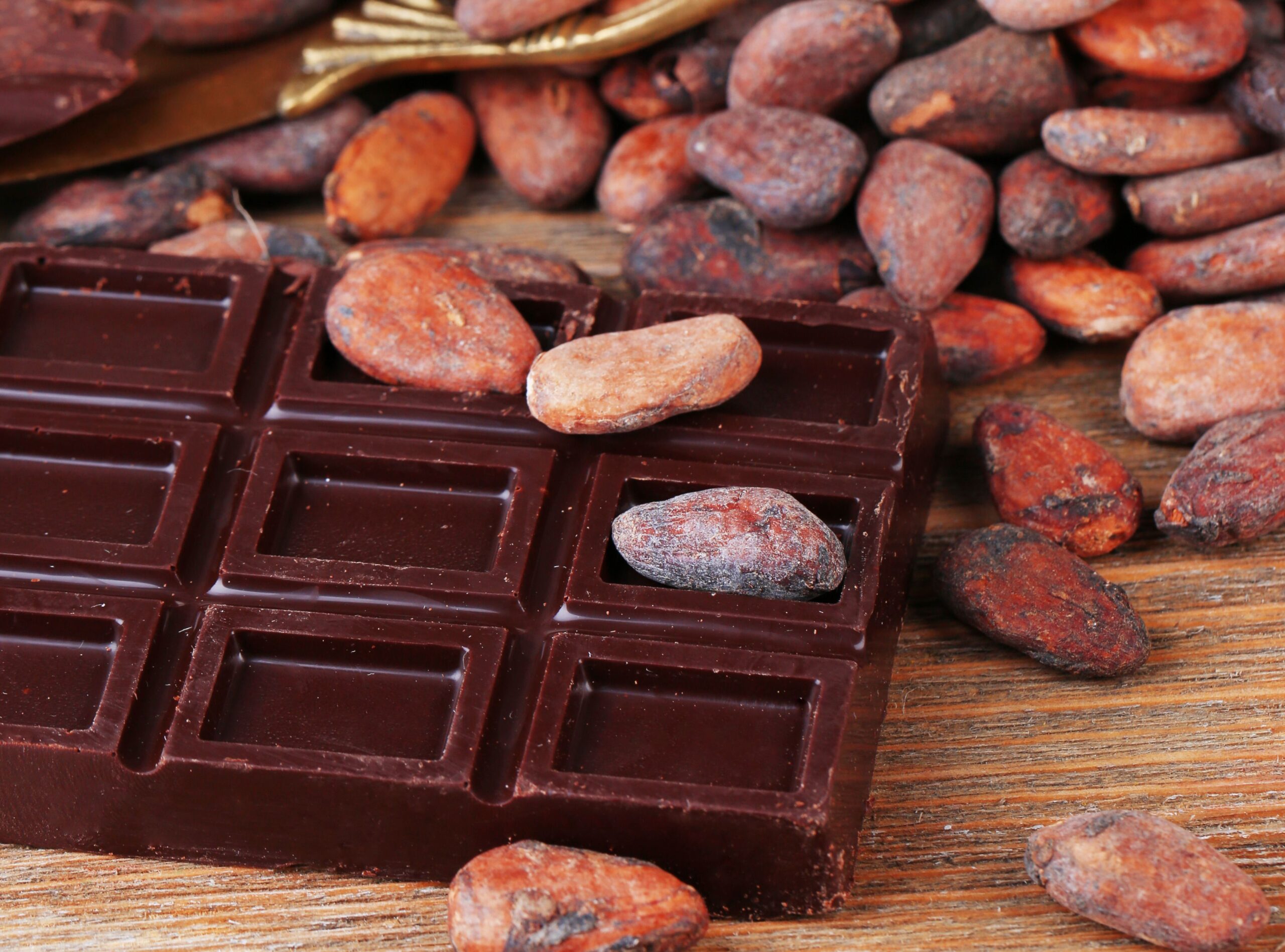 Cracked chocolate bar and cocoa beans on wooden background