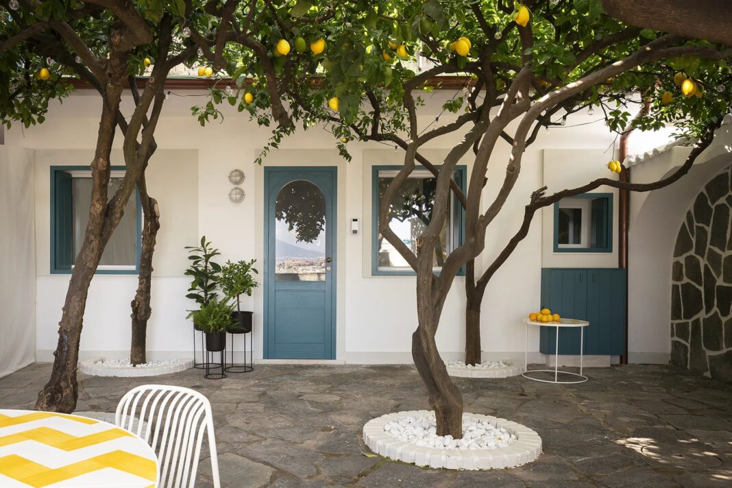 Le finestre blu e la porta della mini casa a Posillipo si affaccia sul patio panoramico con alberi di limoni