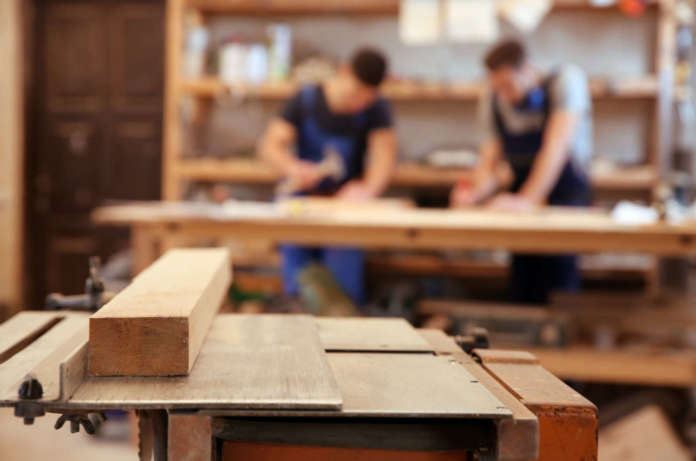 Table in workshop and blurred carpenters on background Agevolazioni alle Pmi rispettose dell'ambiente