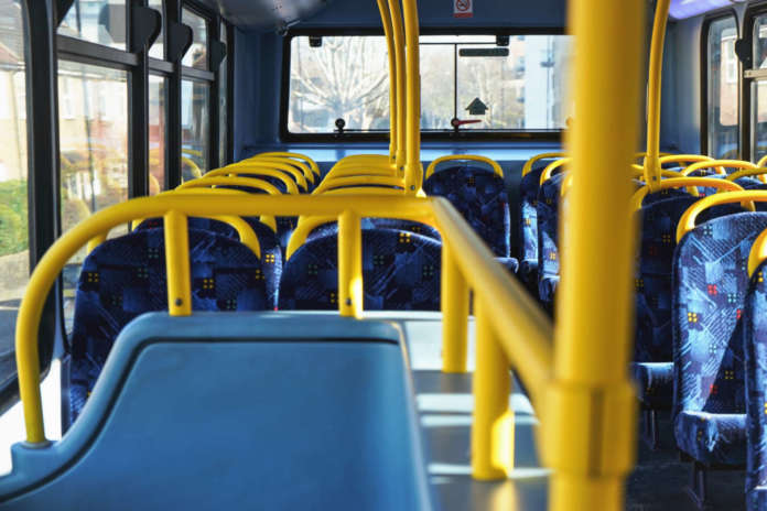 Sun shines on empty interior of London double decker bus, yellow holding rails and blue seats Acquisto di carburante sostenibile