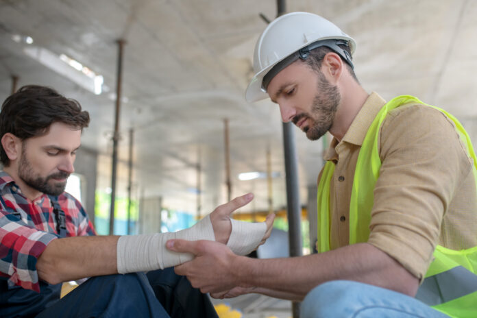 Building worker in helmet applying bandage on his coworker forearm 15 aprile: parte dil bando Isi
