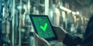Teamsystem Cybersecurity Engineer holding tablet showing green check mark in industrial factory setting