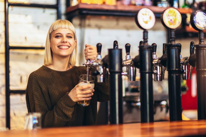 Female bartender tapping beer in bar. Giovani Lavoro