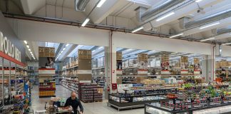 Interno di un cash & carry per bar con ampi scaffali, prodotti food & beverage e un operatore Horeca che rifornisce il carrello