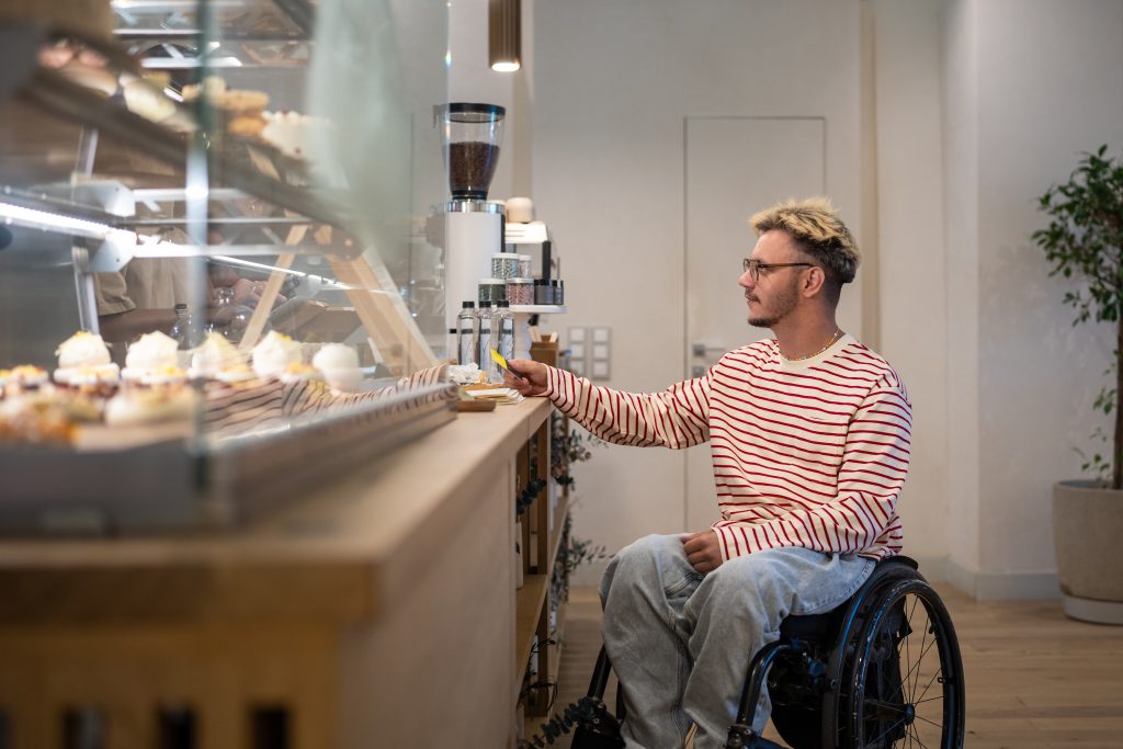 Concentrated disabled man in wheelchair pays for purchase in coffee shop with terminal, credit card