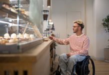 Il tuo locale è davvero inclusivo? Scarica la check list e scoprilo Concentrated disabled man in wheelchair pays for purchase in coffee shop with terminal, credit card