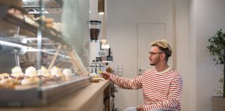 Concentrated disabled man in wheelchair pays for purchase in coffee shop with terminal, credit card