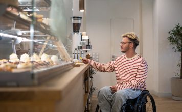 Concentrated disabled man in wheelchair pays for purchase in coffee shop with terminal, credit card