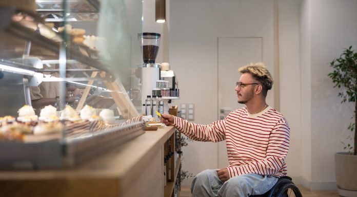 Concentrated disabled man in wheelchair pays for purchase in coffee shop with terminal, credit card