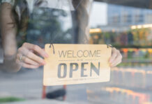 Female store owner turning open sign board of start up coffee shop cafe and restaurant through the door glass and opening the daily service