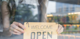 Female store owner turning open sign board of start up coffee shop cafe and restaurant through the door glass and opening the daily service