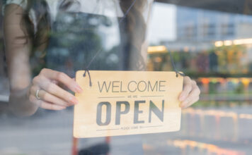 Female store owner turning open sign board of start up coffee shop cafe and restaurant through the door glass and opening the daily service