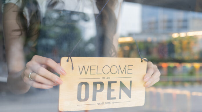 Un locale che funziona in 20 punti chiave Female store owner turning open sign board of start up coffee shop cafe and restaurant through the door glass and opening the daily service