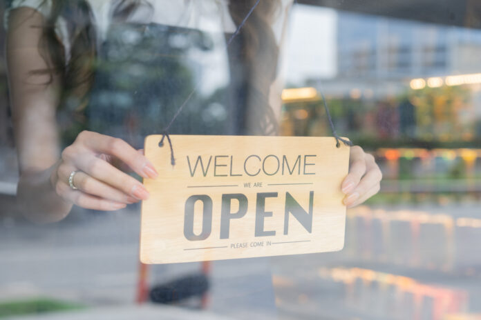 Female store owner turning open sign board of start up coffee shop cafe and restaurant through the door glass and opening the daily service Female store owner turning open sign board of start up coffee shop cafe and restaurant through the door glass and opening the daily service
