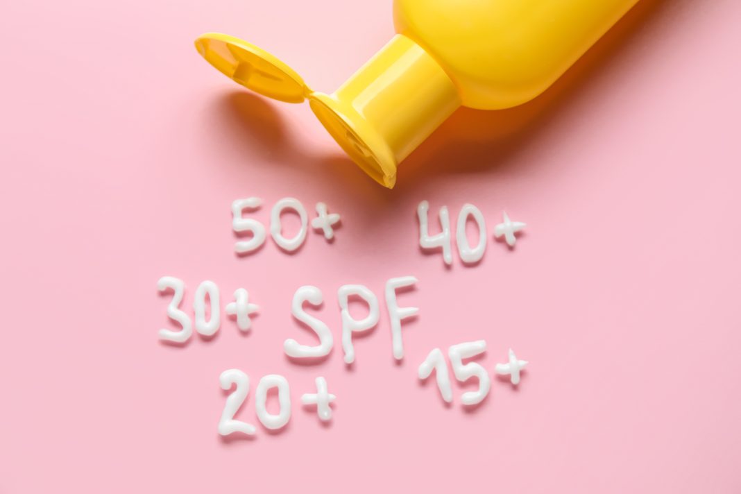 Word SPF and numbers made of cream with bottle of sunscreen on pink background