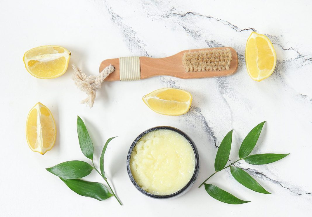 Bowl of lemon body scrub and massage brush on grunge white background