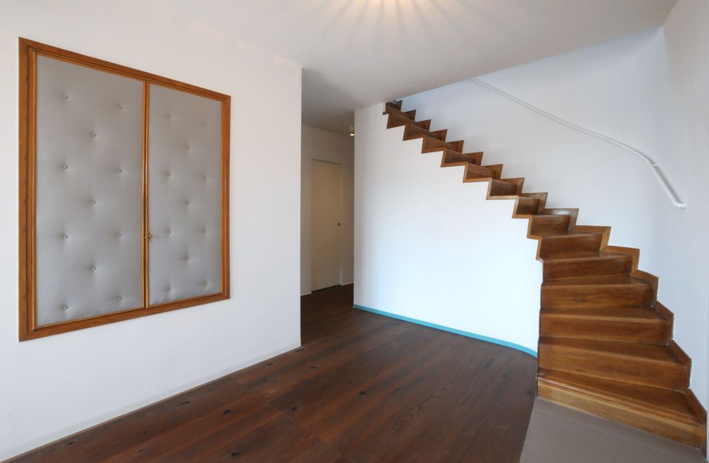 Una vista della scala che conduce all’attico, con corrimano in metallo bianco lucido e uno zoccolo azzurro che segue l’andamento curvo della parete (foto di Angelo Aloisi)