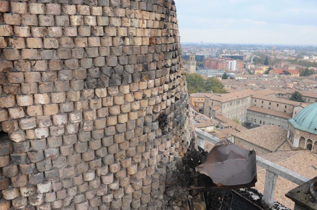La struttura medioevale della cuspide a copertura del fusto del campanile con la peculiare invetriatura a fasce bicrome alternate dai conci in laterizio.