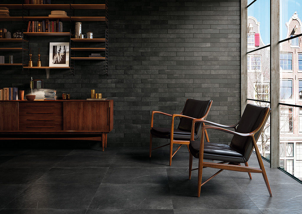 Nella foto, elegante zona living. La parete è realizzata con il rivestimento in gres porcellanato Maku Atelier Dark cm 7,50x30, mentre il pavimento con la versione Matt di Maku Dark in gres porcellanato, nel formato maxi cm 75x75 RT, che offre affascinanti imperfezioni materiche, tipiche della pietra. (foto Fap Ceramiche)