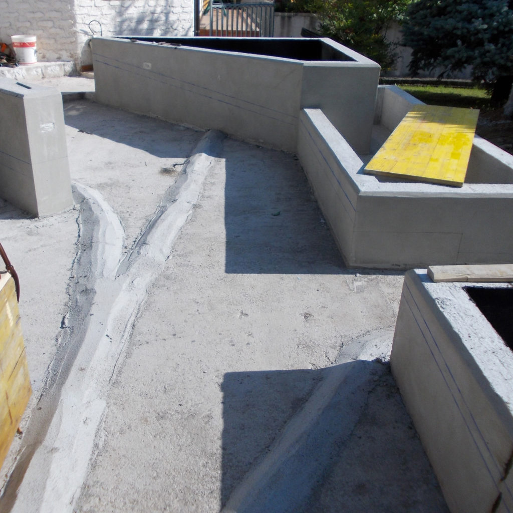 Il basamento in calcestruzzo esistente, che costituisce la base della ripavimentazione. Nella prima fase sono state realizzate le vasche che fungeranno da fioriere o da vasca d’acqua che dal punto di vista costruttivo e funzionale conterranno i percorsi a rampa e caratterizzeranno architettonicamente le aree, altrimenti di “risulta”, all’intersezione dei percorsi.