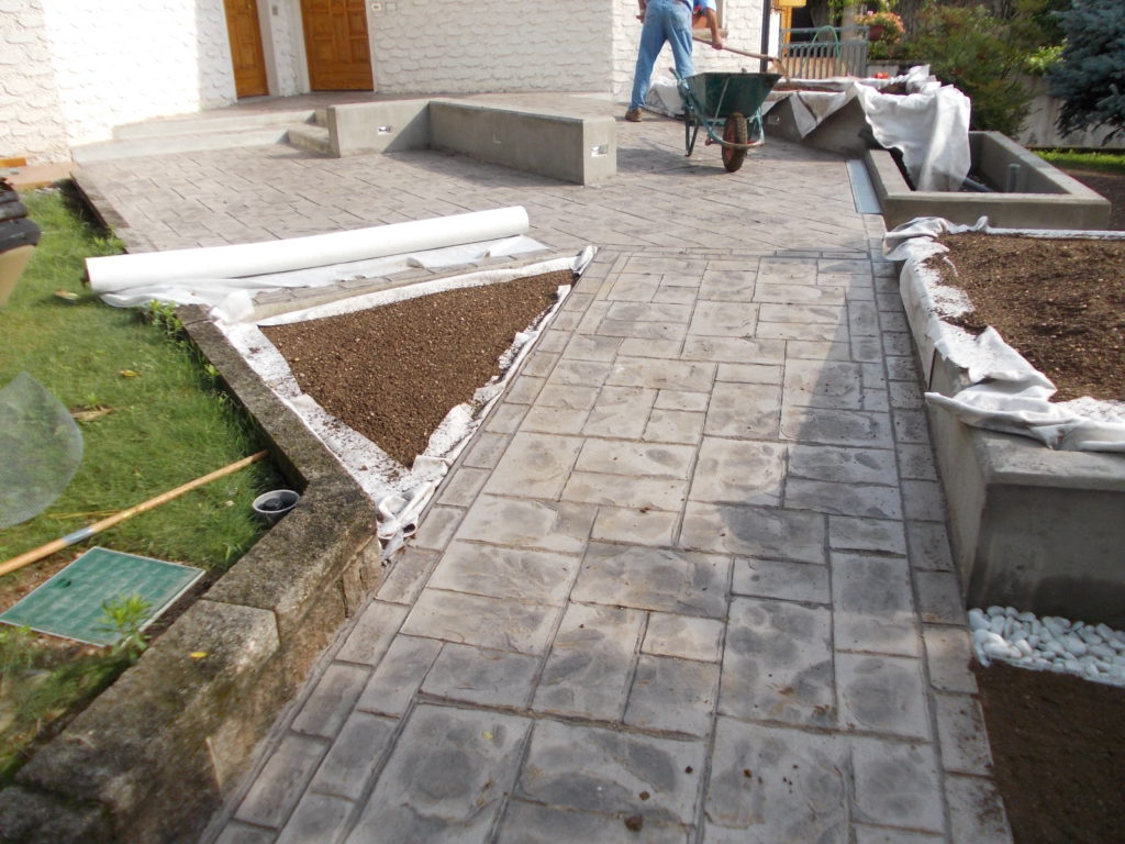 Terminati i lavori del pavimento stampato, sono state riempite di terriccio le fioriere sopra un geotessuto che separa lo strato vegetale da un sottostante strato drenante in ghiaia. Sono stati quindi inseriti i corpi illuminanti nelle rispettive controcasse. Sono quindi state posate le lastre in pietra piasentina flexata che fungono da copertina alle vasche e da seduta al muretto della panca. Su tutti i bordi delle vasche in calcestruzzo è stata creata una scanalatura rientrante che disegna un distacco, un segno e una linea d’ombra tra i due materiali calcestruzzo e pietra. 