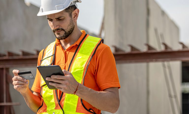 Operaio in cantiere con elmetto e gilet riflettente, effettua con tablet e carta di credito pagamenti digitali che nelle imprese edili ottimizzano la gestione