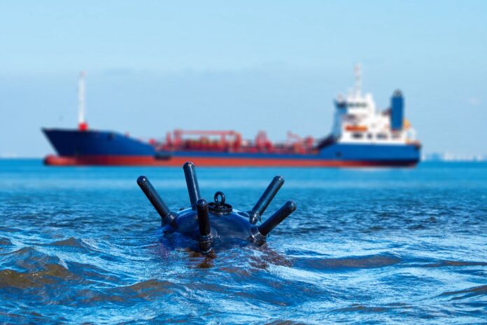 Sea mine floats in water. Anti-ship bomb in ocean. Civilian ship sails past sea mine. Mined sea area. Anti-ship mine for maritime security. Bomb for creating marine blockade. Art focus mine Hormuz