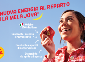 Joya®, la mela rossa italiana alla conquista dei mesi caldi Giovane donna sorridente che tiene in mano una Joya® mela rossa italiana, simbolo di freschezza, croccantezza e origine 100% italiana, sotto un cielo estivo azzurro.