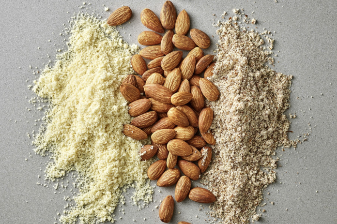 Farina e semola di mandorle Tre tipologie di farina e semola di mandorle: farina di mandorle fine a sinistra, mandorle intere al centro e semola di mandorle grossolana a destra su sfondo grigio