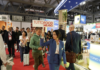 Interno dei padiglioni di TUTTOFOOD 2026 a Rho Fieramilano con visitatori tra gli stand e hostess che sorregge il cartello ufficiale della manifestazione