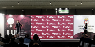 Un oratore parla dal podio durante una conferenza ufficiale a LUV Fiera dell'uva da tavola a Bari, con un grande fondale brandizzato e il logo della Regione Puglia sullo sfondo, davanti a una platea di operatori del settore
