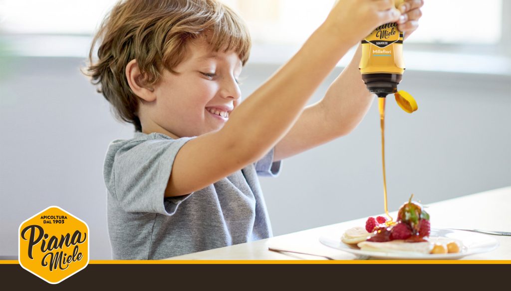 Bambino che aggiunge miele a un piatto utilizzando lo Squeeze Piana Miele