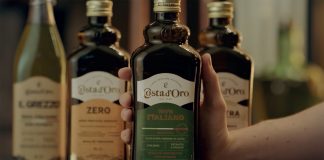 Bottiglia di olio extravergine di oliva Costa d’Oro 100% Italiano tenuta in mano, con altre referenze della linea sullo sfondo
