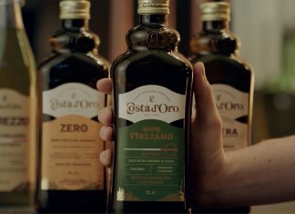 Costa d’Oro: passione per l’innovazione e fedeltà alla terra Bottiglia di olio extravergine di oliva Costa d’Oro 100% Italiano tenuta in mano, con altre referenze della linea sullo sfondo