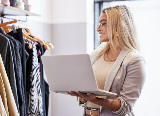 La customer experience nasce nel magazzino del negozio Addetta alla gestione magazzino in un negozio di abbigliamento controlla lo stock tramite laptop davanti a una fila di vestiti