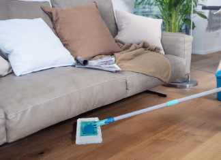 Superduster Leifheit in azione mentre pulisce sotto un divano, ideale per la rimozione della polvere su pavimenti in legno in modo sostenibile