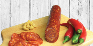 Tagliere di legno con fette di salumi piccanti Sant’Orso, peperoncini rossi e verdi e un mix di frutta secca