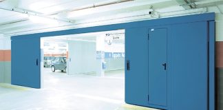 Chiusura tecnica FAAC manutenuta da Techno-Fire: porta tagliafuoco scorrevole con portina integrata in autorimessa GDO, segnaletica di uscita visibile