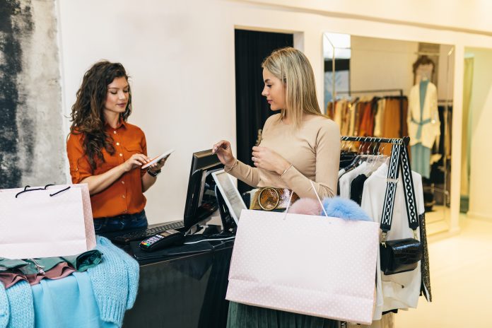 Commessa e cliente in negozio di abbigliamento durante il pagamento alla cassa, rappresentazione della gestione degli incassi nel punto vendita