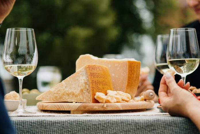 Punta e scaglie di formaggio su un tagliere con calici di vino, immagine evocativa della presenza di Parmigiano Reggiano a Marca 2026.