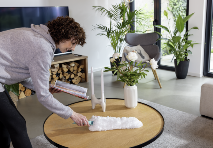 Una donna utilizza lo spolveratore Leifheit Superduster su un tavolo in legno per una pulizia casa sostenibile e profonda senza l'uso di prodotti chimici