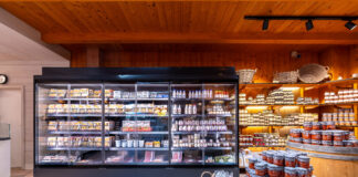 Un moderno banco frigo professionale a sportelli in un negozio di gastronomia, esempio di refrigerazione AHT Italia per l'esposizione di prodotti freschi e latticini
