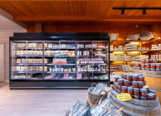Un moderno banco frigo professionale a sportelli in un negozio di gastronomia, esempio di refrigerazione AHT Italia per l'esposizione di prodotti freschi e latticini