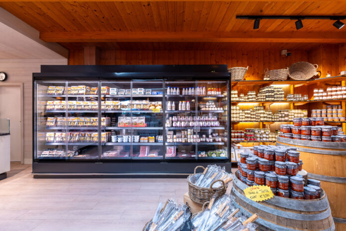 Un moderno banco frigo professionale a sportelli in un negozio di gastronomia, esempio di refrigerazione AHT Italia per l'esposizione di prodotti freschi e latticini
