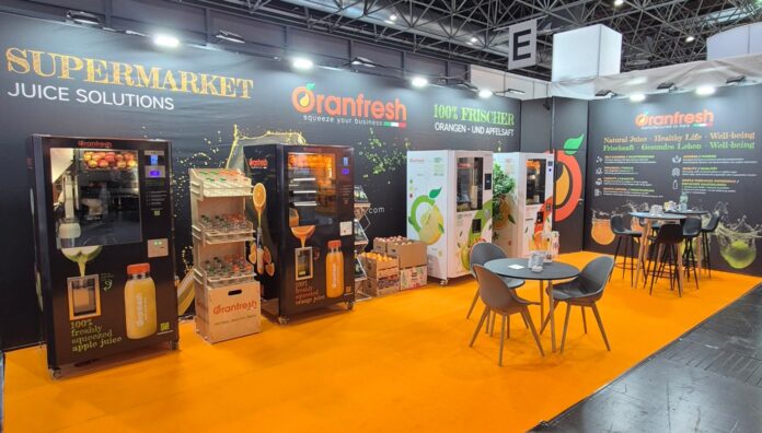 Oranfresh Euroshop 2026 Stand fieristico di Oranfresh a Euroshop 2026 con pavimentazione arancione, macchine per spremute fresche, espositori di arance e tavoli da bar