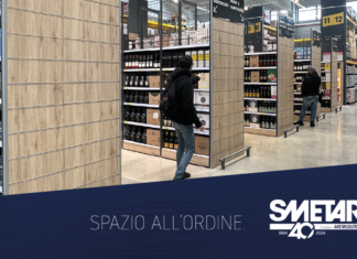Un corridoio di supermercato allestito con scaffalature moderne Smetar con finiture in legno, piene di bottiglie di bevande alcoliche. Due persone osservano i prodotti, mostrando l’efficienza dell'organizzazione degli spazi espositivi per la GDO. In basso a destra è visibile il logo Smetar 40 Gruppo Metalsistem