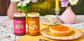 Due vasetti di confettura Darbo 80% frutta ai gusti lampone e albicocca su una tavola imbandita per la colazione con pane tostato, fiori freschi e un'atmosfera naturale e solare
